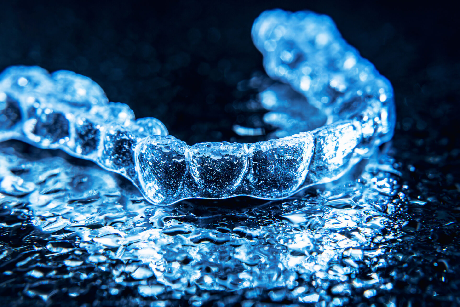 Transparent Aligners, Tooth Retainers Lie On A Mirror With Water Droplets On A Black Background Transparent Aligners, Tooth Retainers Lie On A Mirror With Water Droplets On A Black Background